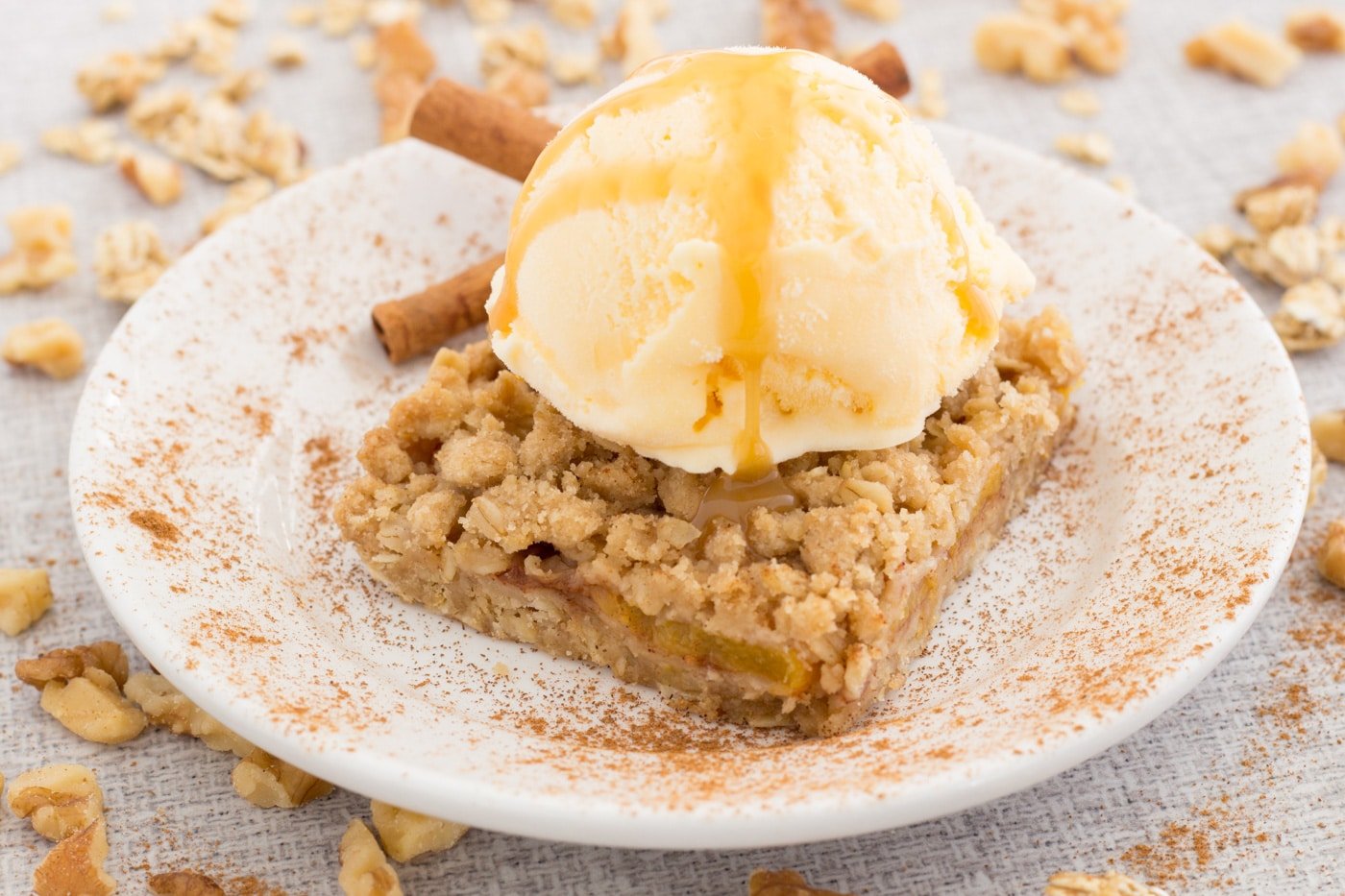 peach bars with ice cream and caramel sauce on a white plate sprinkled with cinnamon