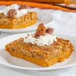 Slices of pumpkin crunch cake topped with whipped cream and candied pecans on white plates