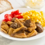 beef and noodles on a plate with yellow corn and cherry tomatoes