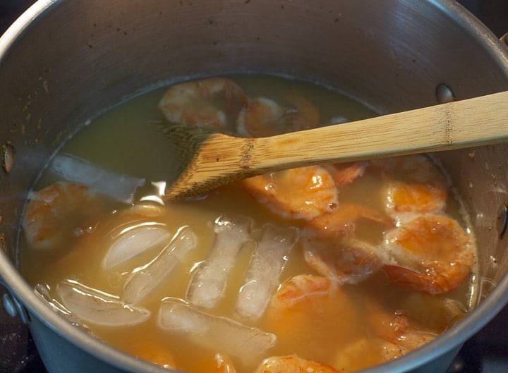 Cooked shrimp and ice cubes in a pot of broth with a wooden spoon