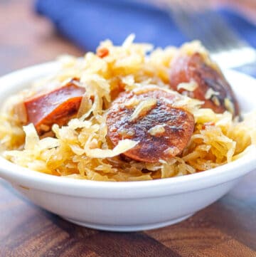 Browned kielbasa with sauerkraut in a white bowl sitting on a wooden board