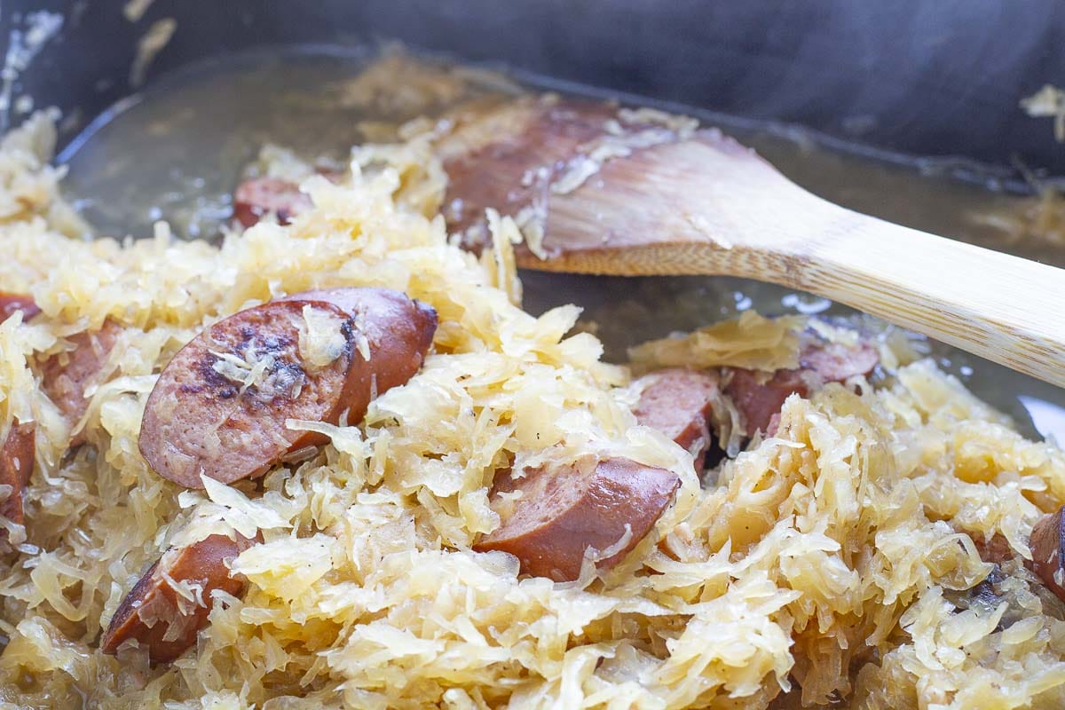 Sauerkraut and sausage in an electric skillet with a wooden spoon