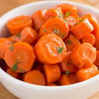 Candied carrots topped with parsley in a white bowl
