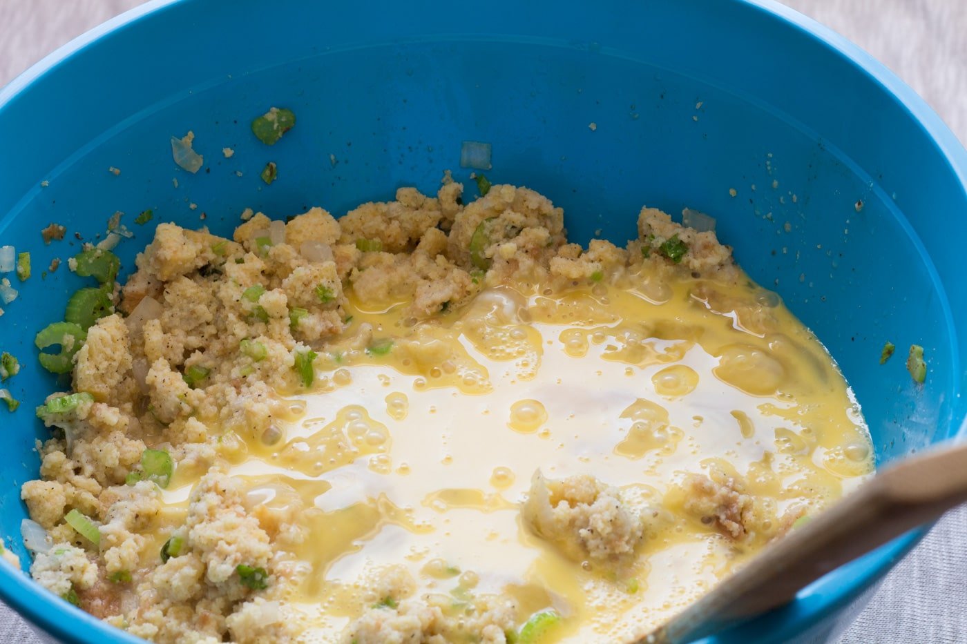 Cornbread dressing mix covered with raw beaten eggs in a blue bowl