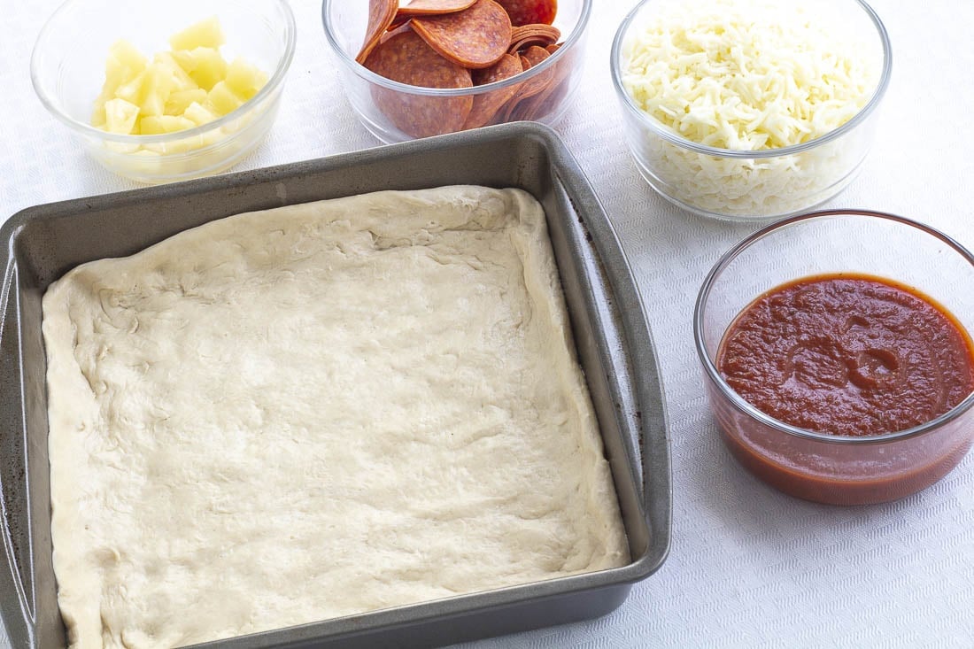 Deep Dish crust in a baking pan surounded by pizza toppings