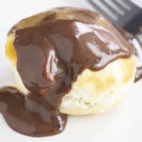 Close up view chocolate gravy covered biscuit with a fork on a white plate