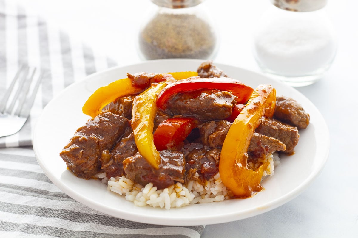 Pepper steak served over rice on a white plate and grey striped napkin