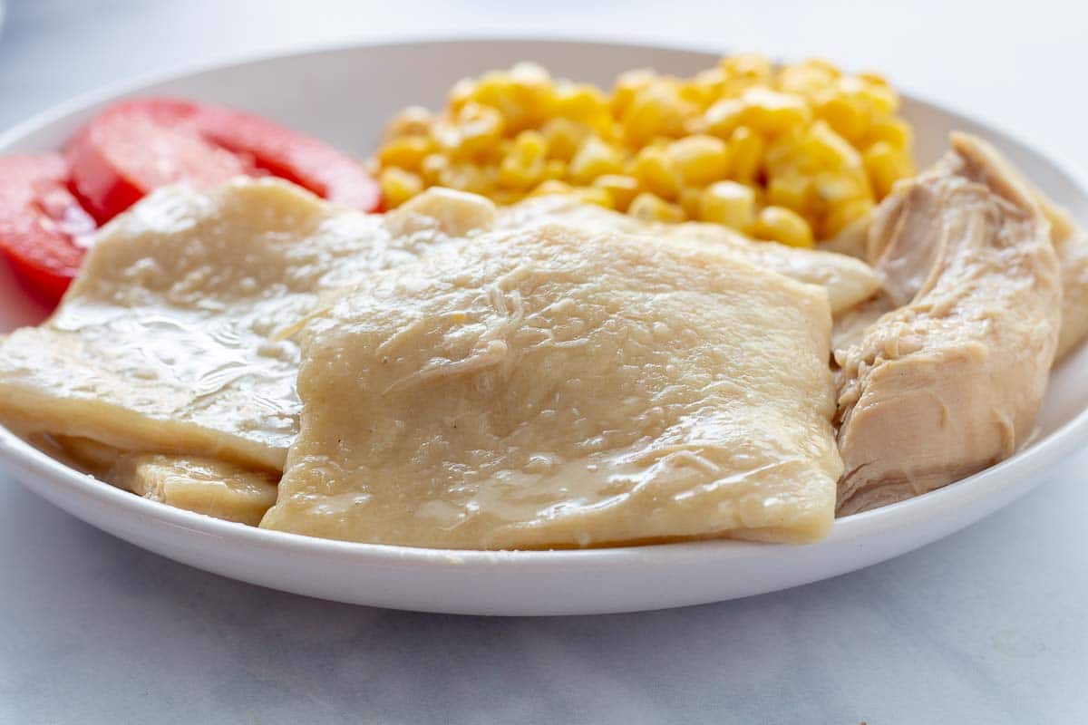 Southern dumplings on a plate with chicken, corn, and tomato slices.