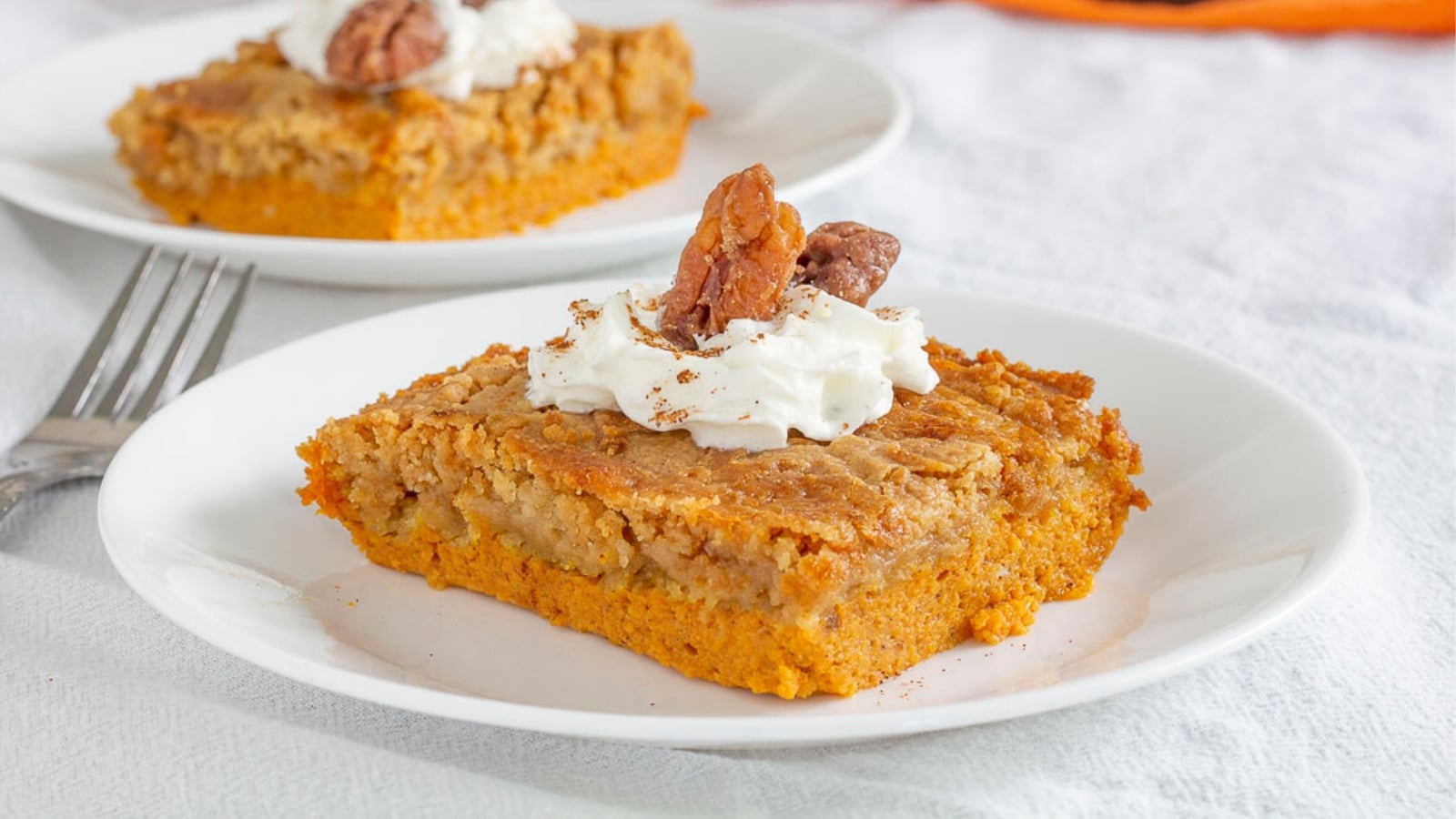 Pumpkin dump cake slices  topped with whipped cream and candied pecans on plates
