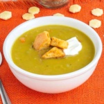 Pea soup in a white bowl topped with croutons and sour cream