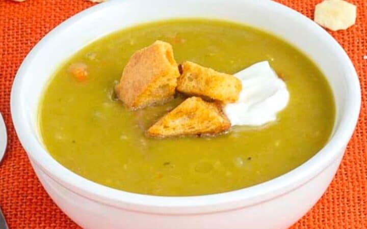 Pea soup in a white bowl topped with croutons and sour cream