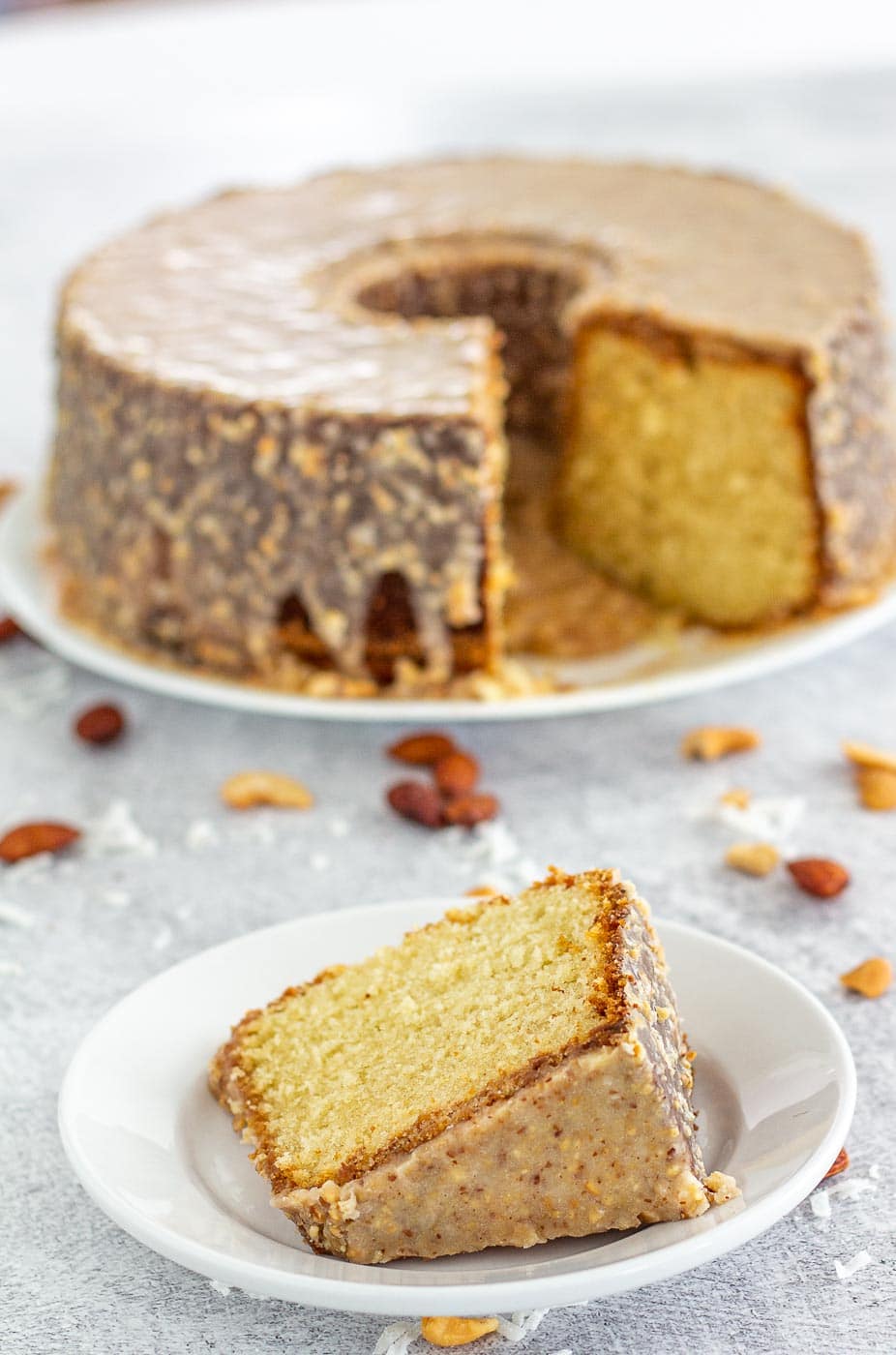 Slice of crunch cake with a crunchy glaze on a plate with a cake on a stand in the background.