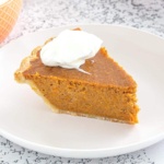 Sweet potato pie topped with whipped cream on a white plate