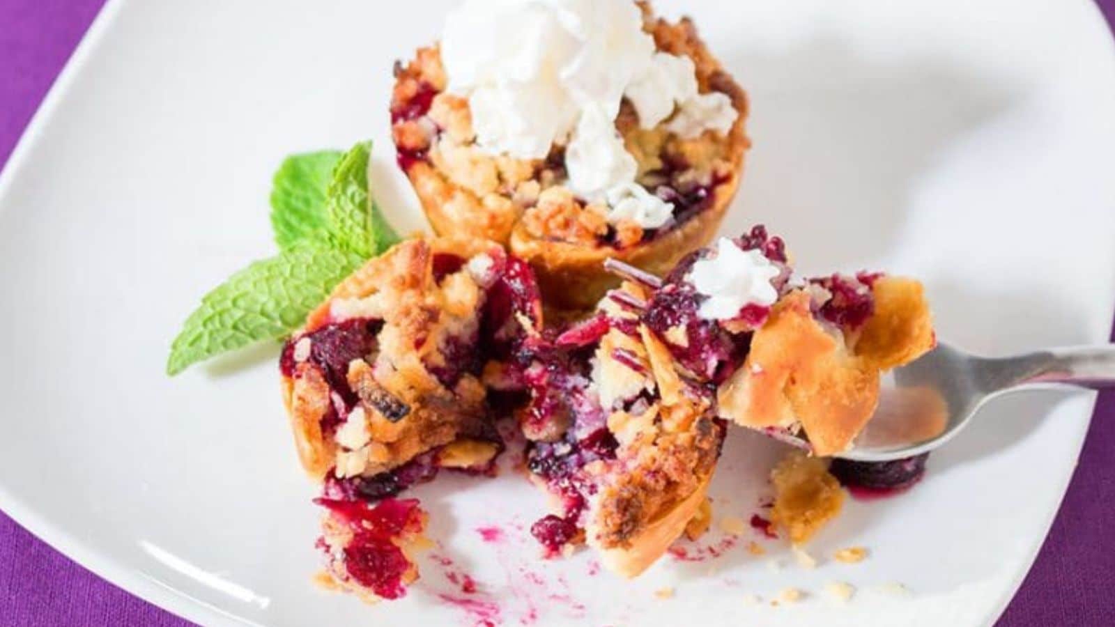 Blueberry tarts on a plate with a fork and a sprig of mint