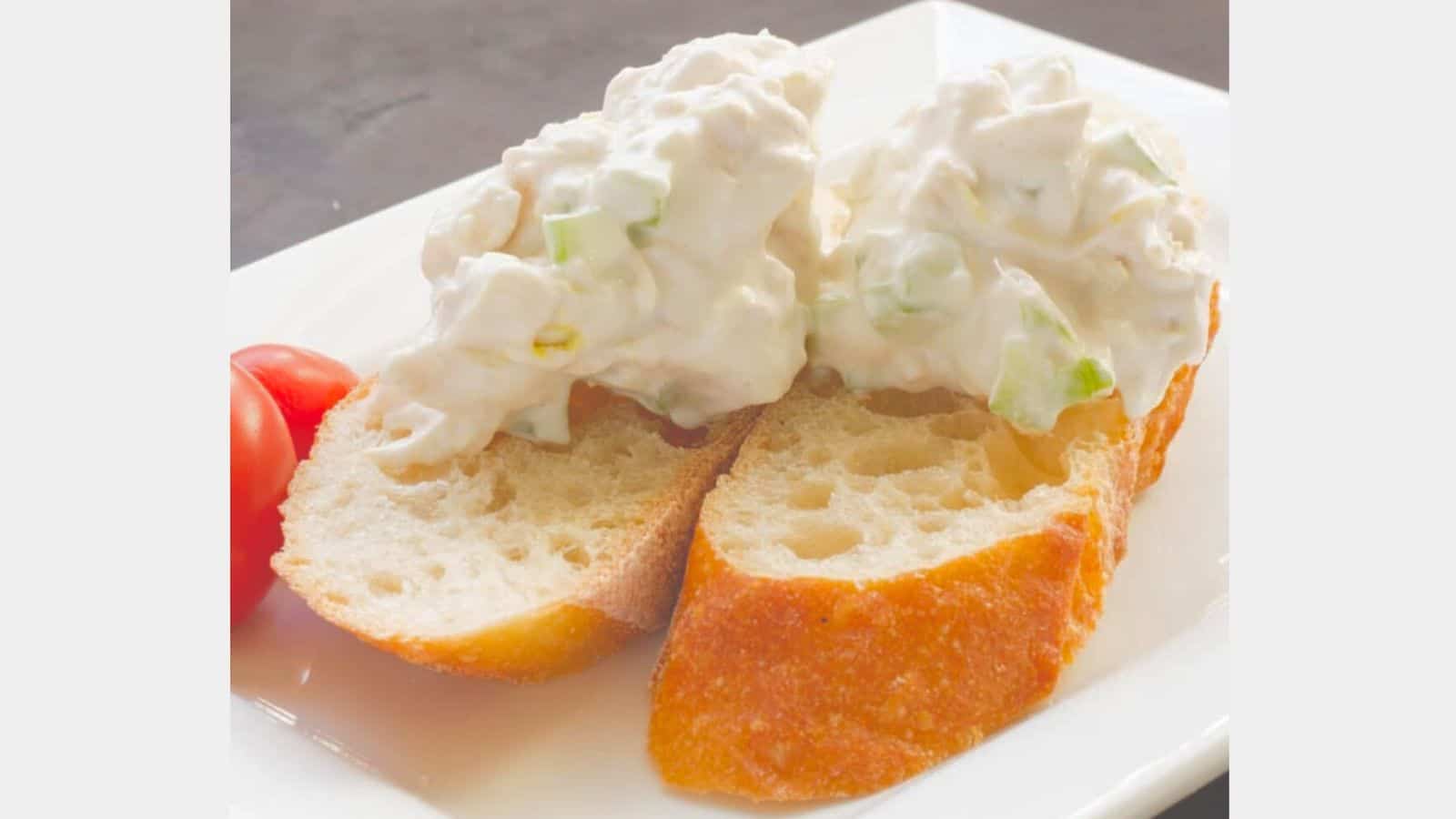 sliced bread topped with creamy chicken salad on a plate with tomatoes