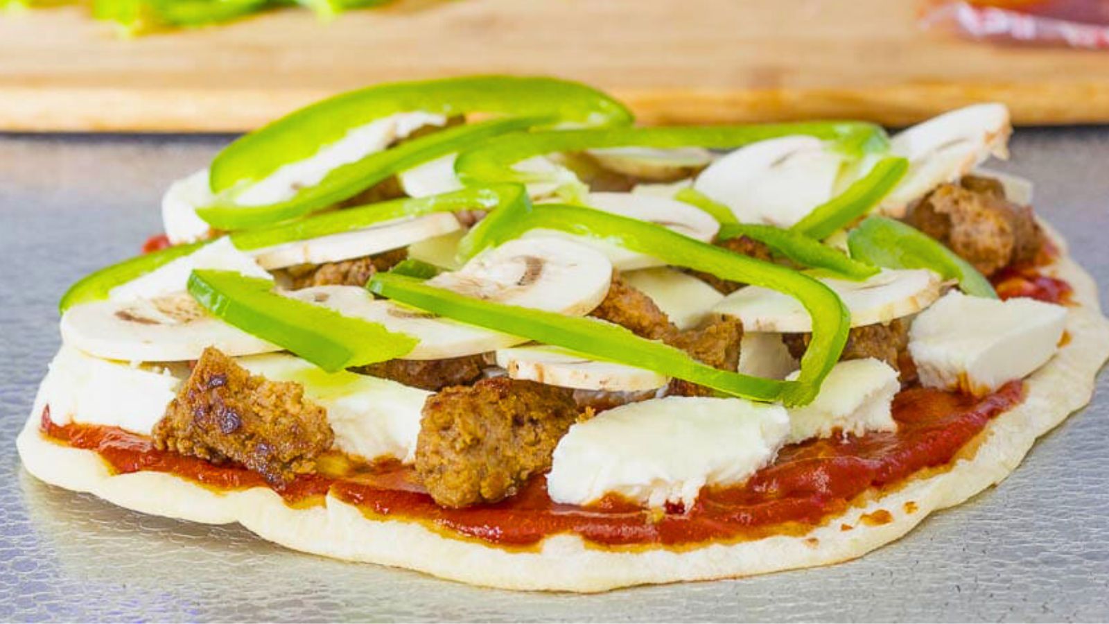 Flatbread covered with cheese, Italian sausage, mushroom and green pepper slices on a baking sheet