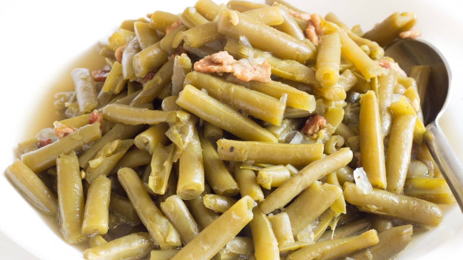 Green beans with bacon pieces in a bowl with a spoon