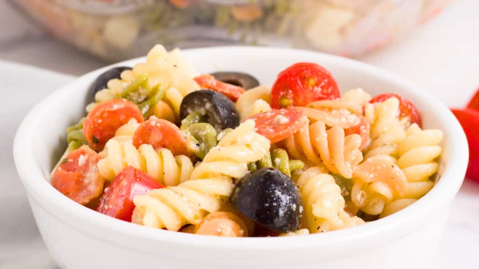 Tricolor rotini black olives pepperoni and tomatoes in a bowl