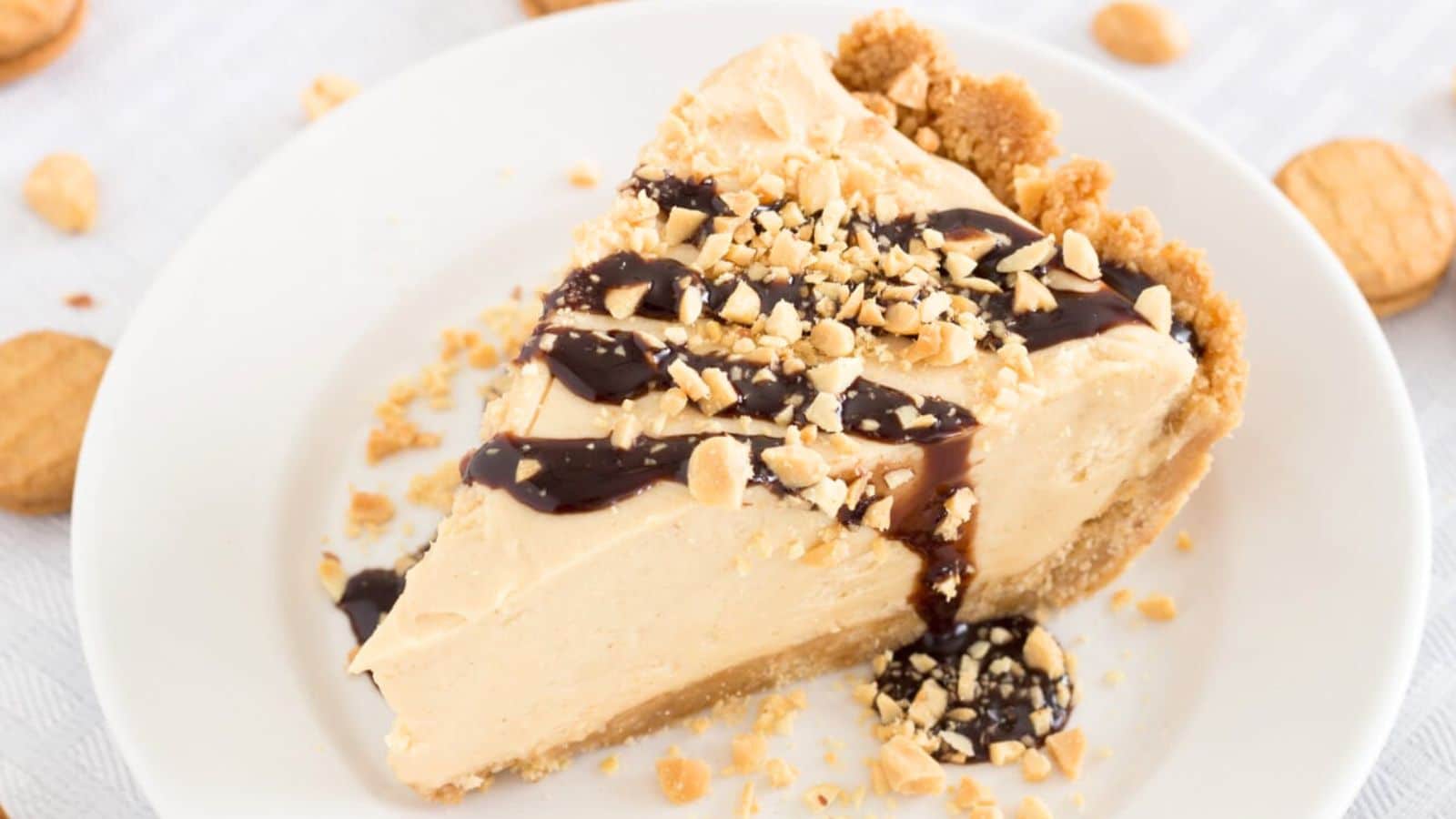 Slice of peanut butter pie topped with chocolate sauce and crushed peanuts on a plate