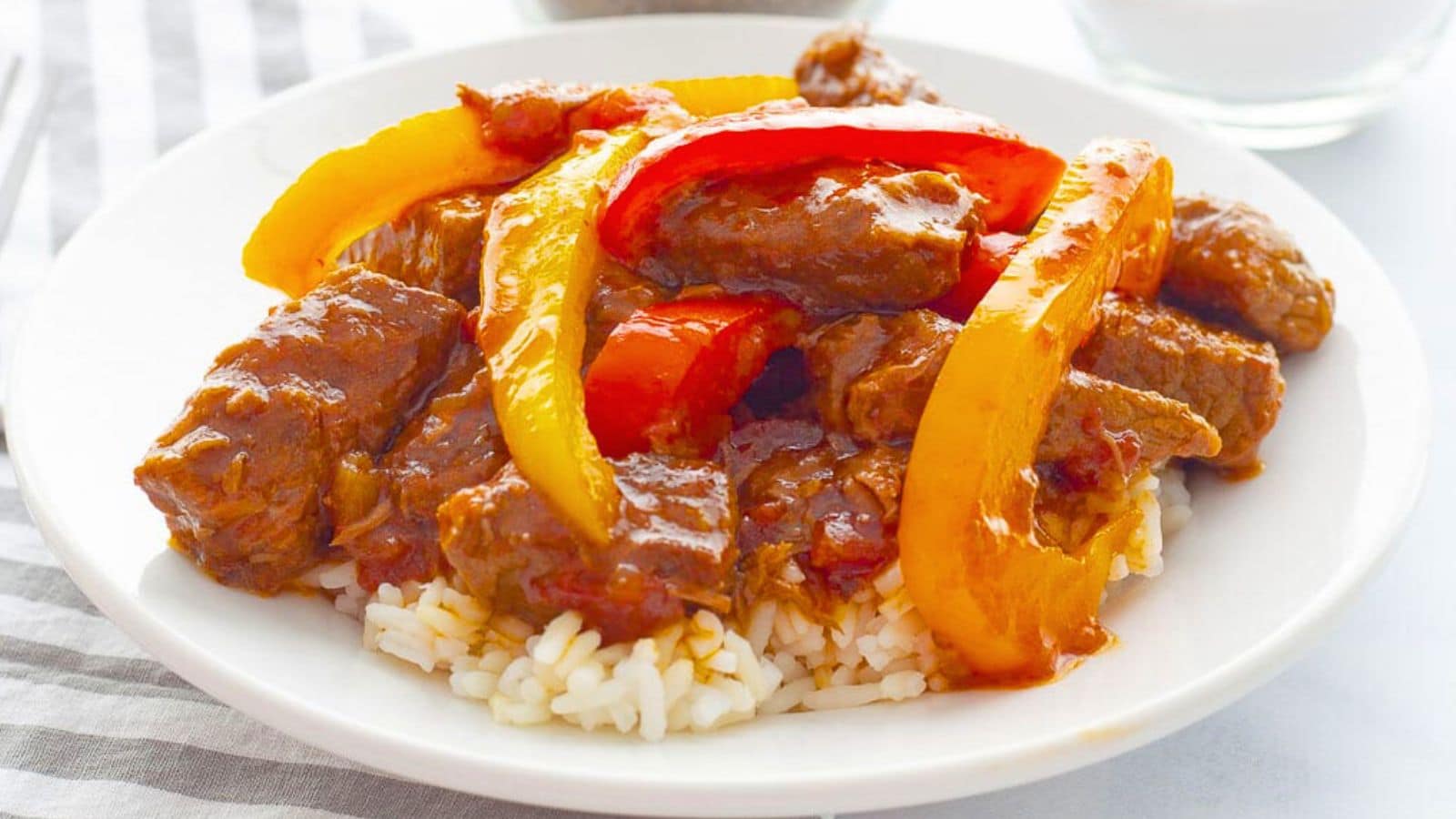 Beef strips with bell peppers over rice on a plate