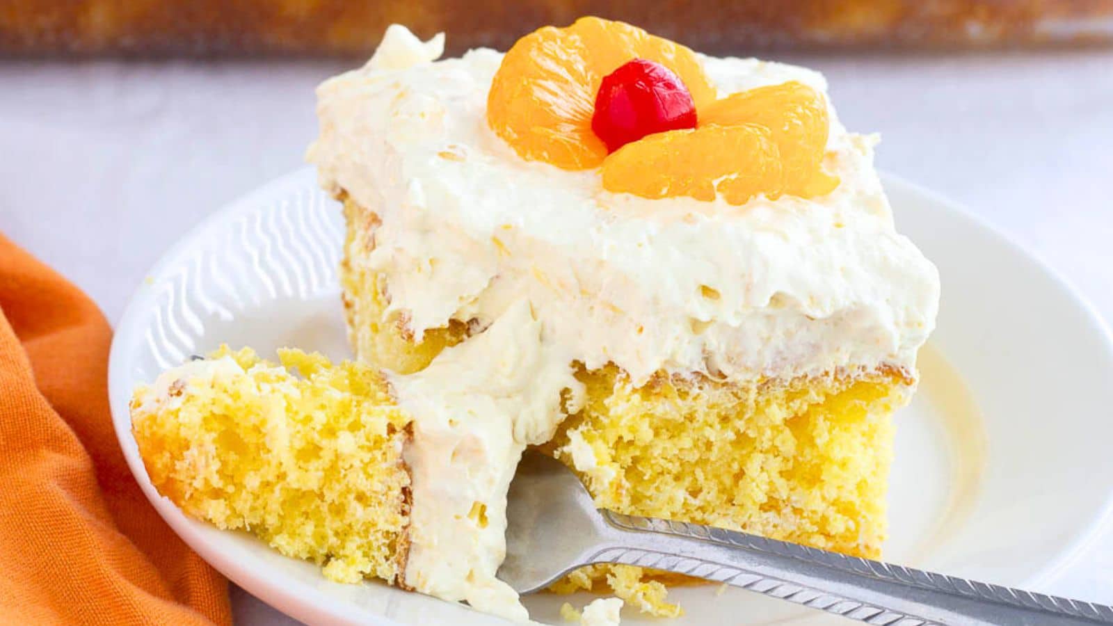 Cake topped with frosting mandarin oranges and a cherry with a bite on a fork