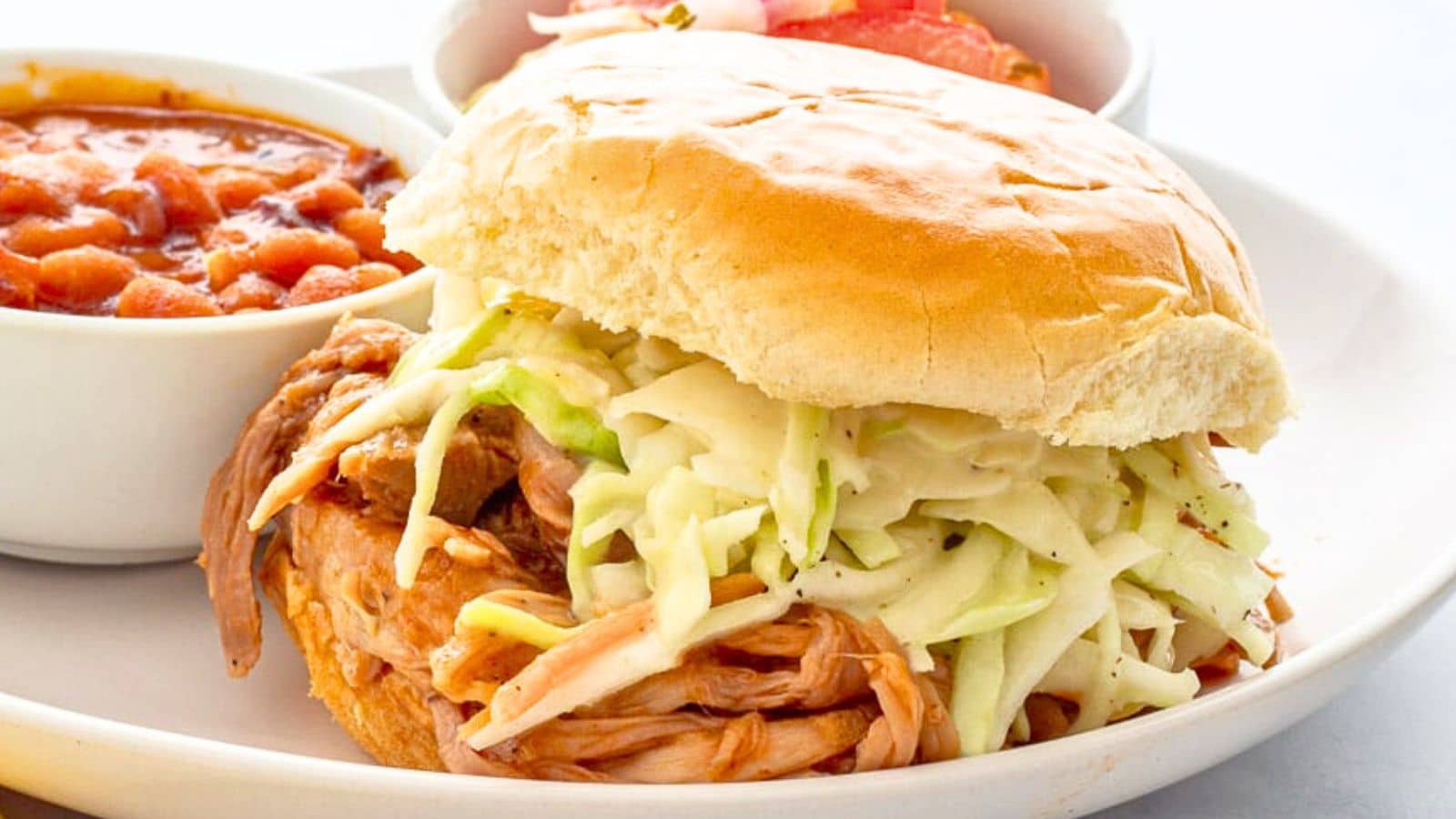 Hamburger bun with shredded pork cole slaw on a plate with beans