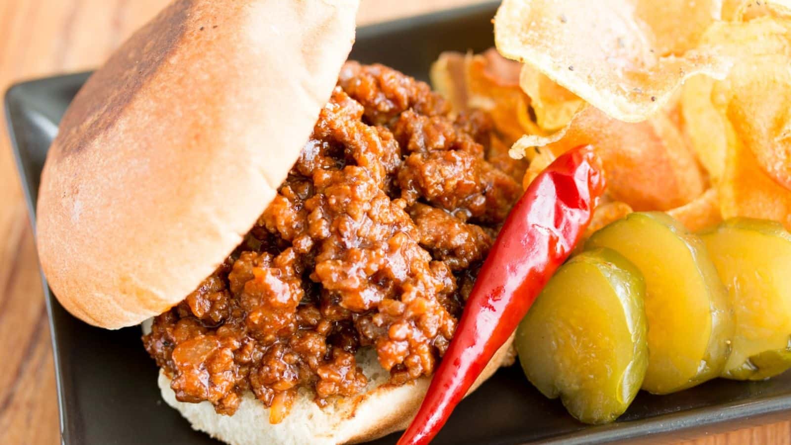Sloppy Joe on a plate with a hot pepper pickles and chips