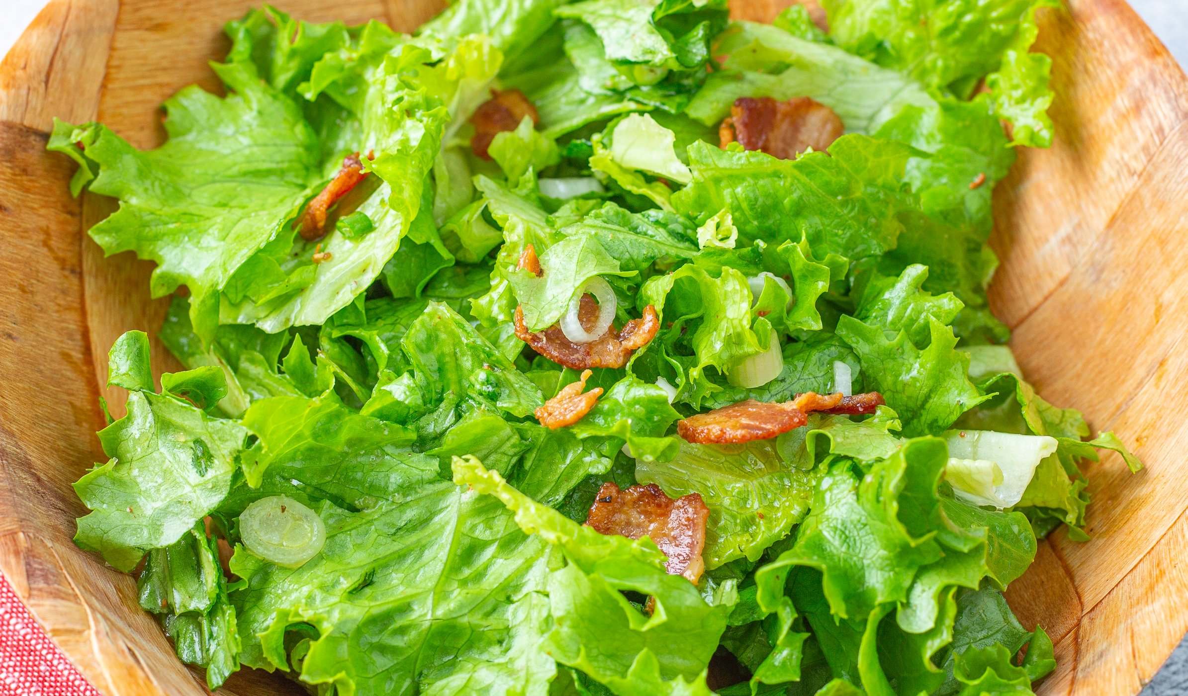 Wilted salad with bacon pieces in a wooden bowl