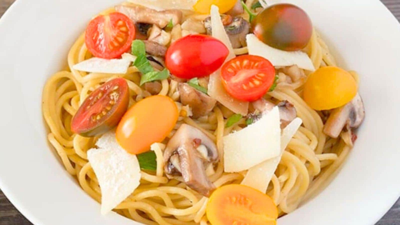 Garlic pasta topped with cheese mushrooms and cherry tomatoes in a bowl