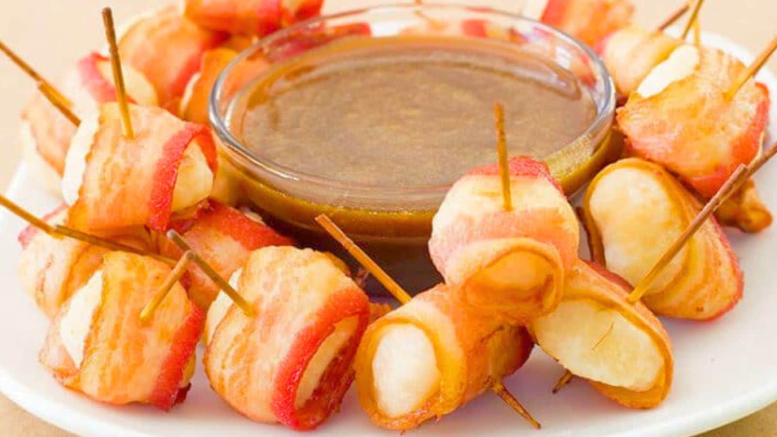 Water chetnuts wrapped in bacon on a plate with sauce in a bowl