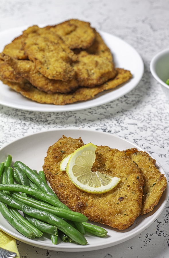 chicken cutlet topped with a lemon slice with green beans on a plate