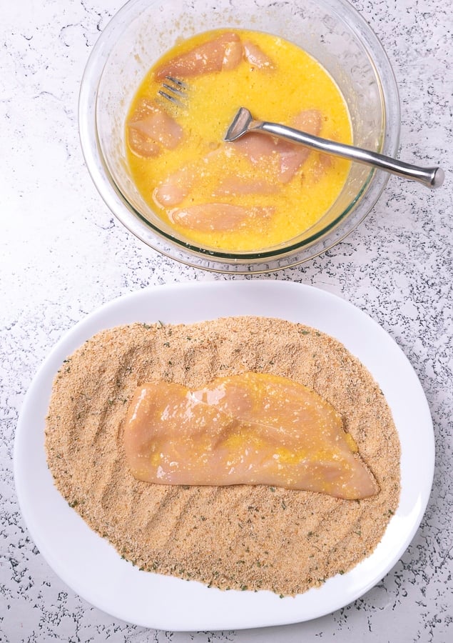 bowl of egg wash and chicken and chicken coated in egg on top of breadcrumbs
