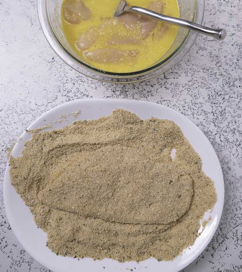 chicken in breadcrumbs under a bowl of egg wash
