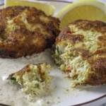 crab cakes on a plate with a bite cut off on a plate with remoulade ad lemon wedges