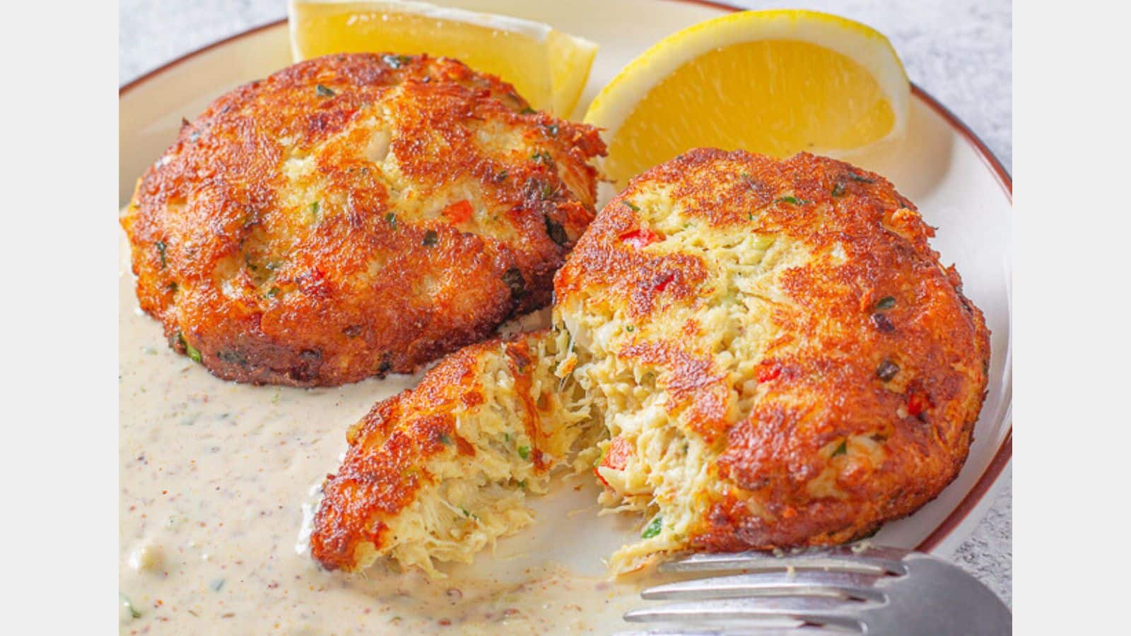 Crab cakes with remoulade sauce lemons and a fork on a plate
