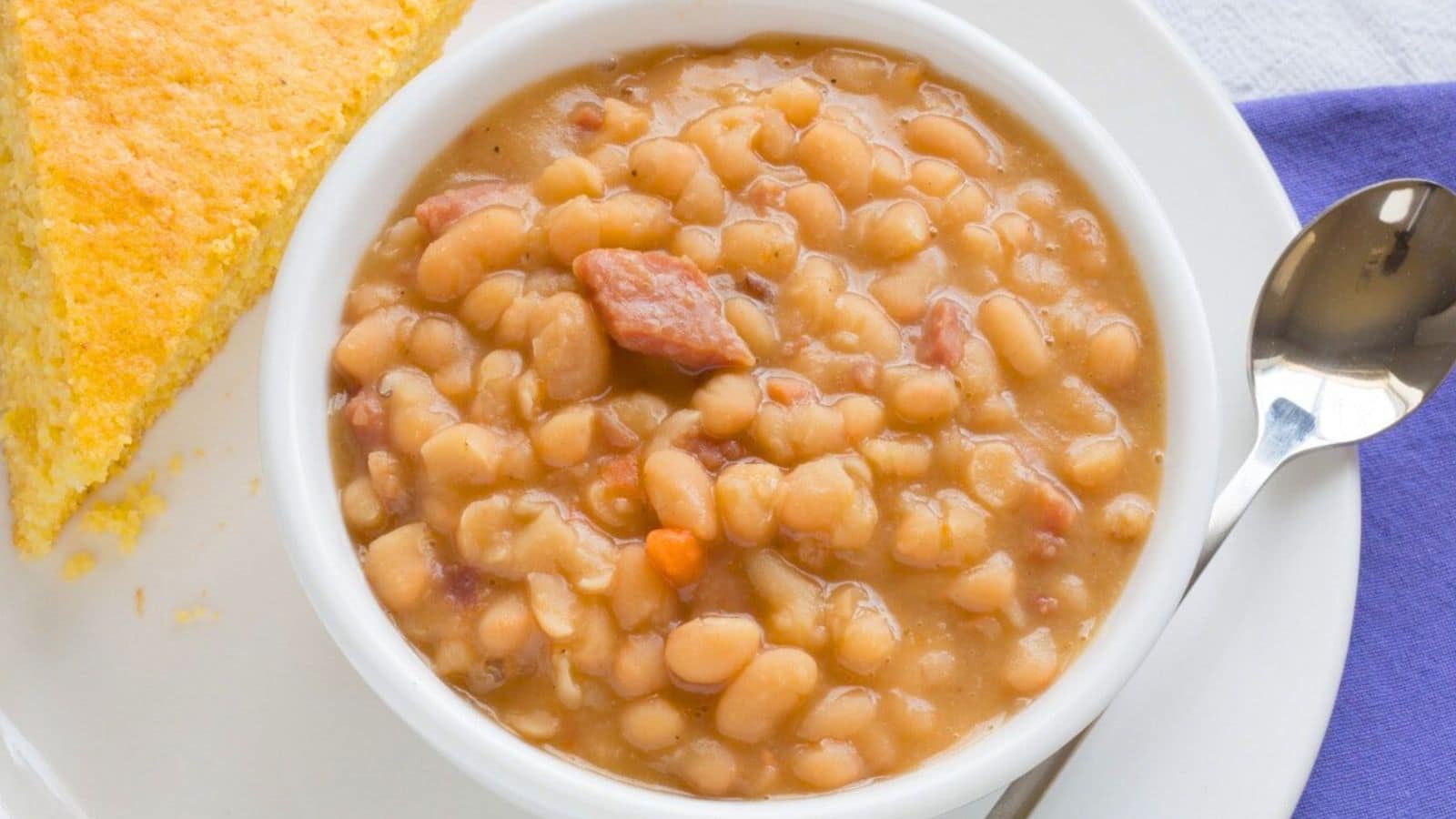 Ham and Beans in a bowl next to a napkin and spoon