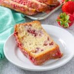 Slice of strawberry pound cake on a plate with more slices and strawberries in the background