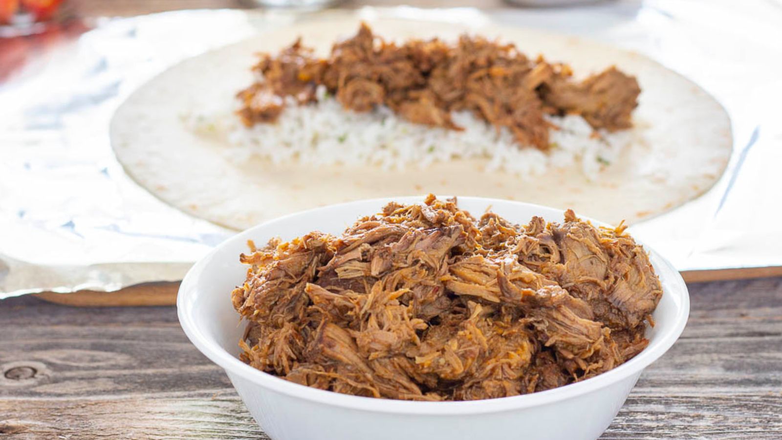 Shredded beef in a  bowl in front of a burrito being made