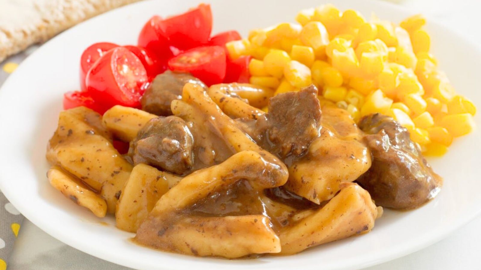 Beef and noodles on a plate with corn and cherry tomatoes