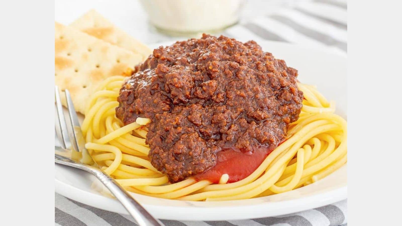 chili beef and spicy ketchup topped spaghetti on a plate with crackers and a fork