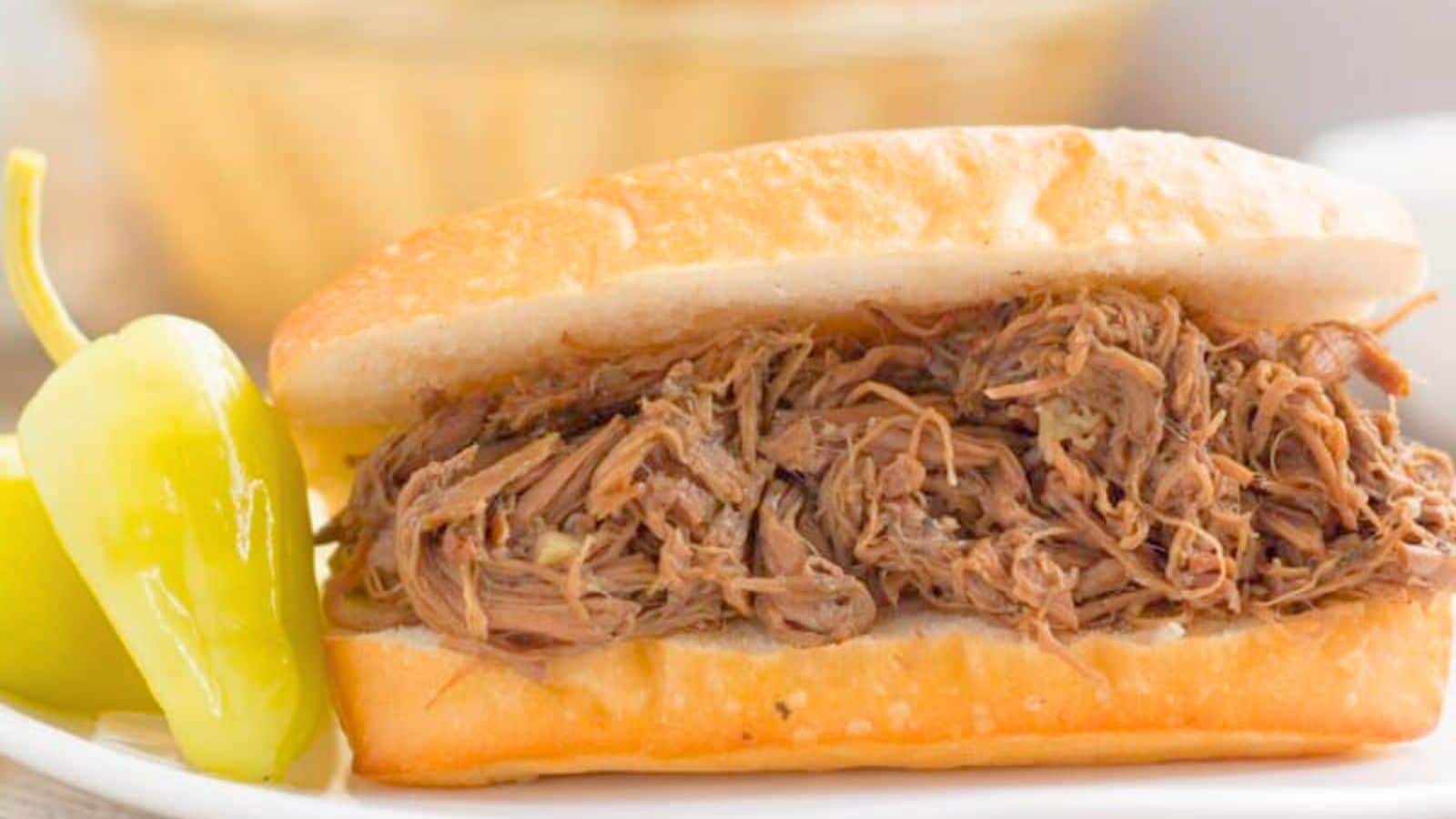 Shredded Italian beef on a bun next to hot peppers