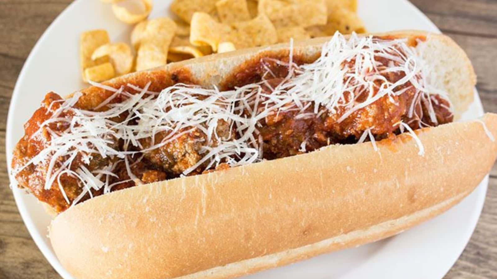 Meatball sub topped with cheese on a plate with corn chips