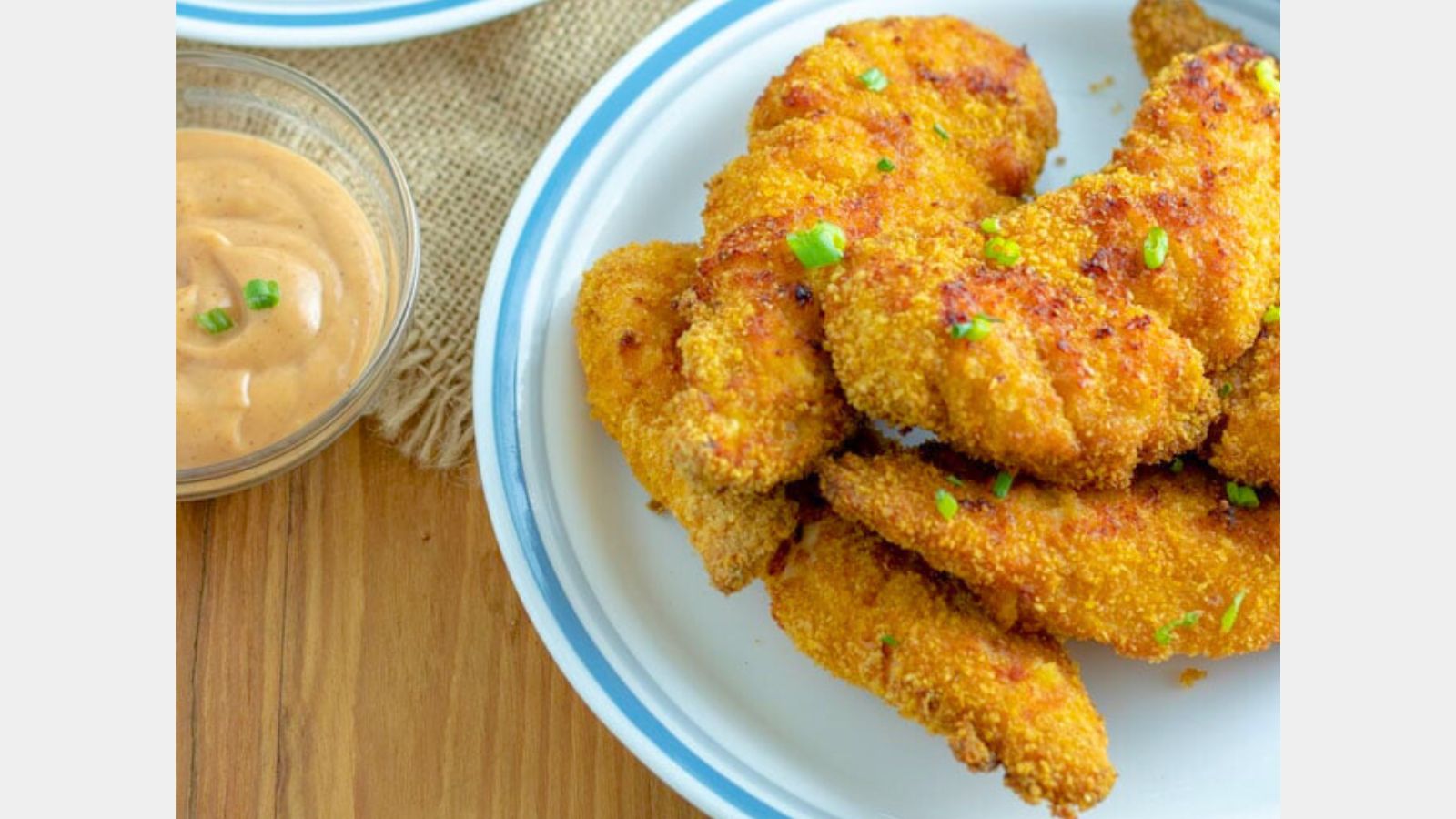 Chicken tenders on a plate sprinkled with green onions next to a small bowl of sauce