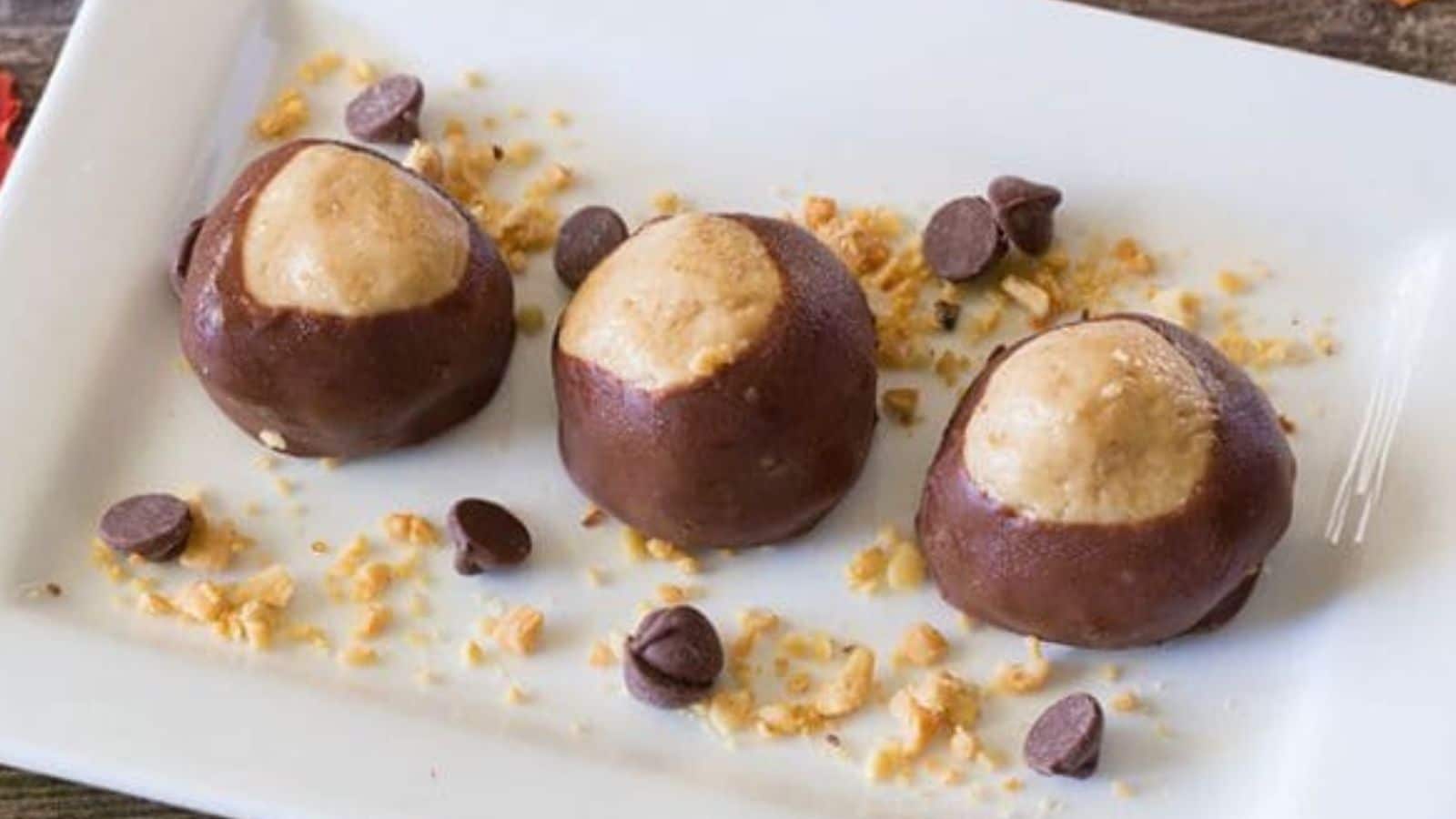 3 buckeye candies on a plate with crushed peanuts and chocolate chips