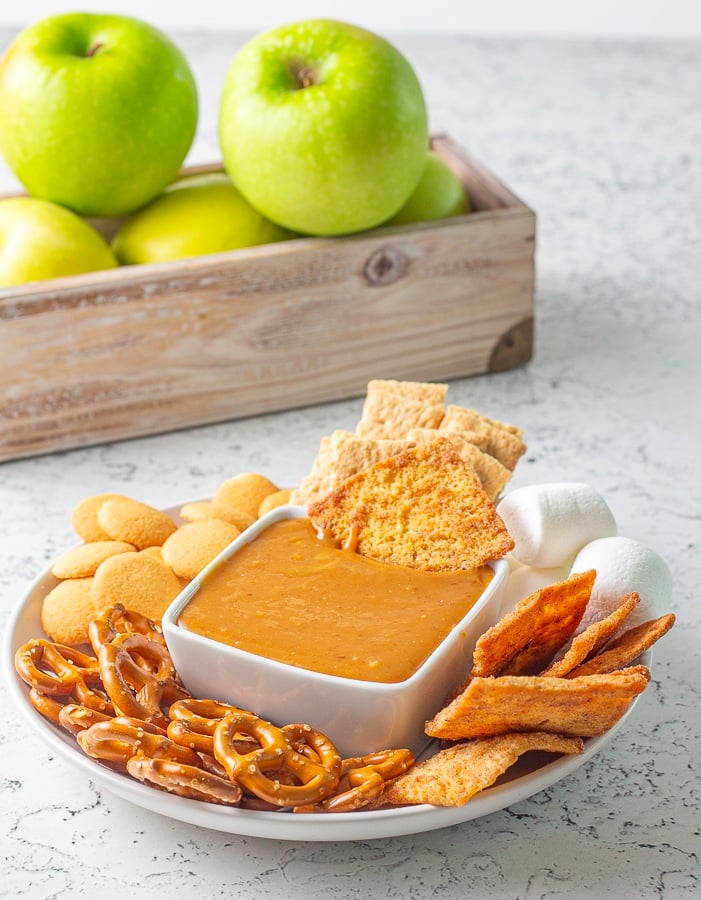 Caramel dip in a bowl surrounded by pretzels cookies marshmallows and cinnamon chips