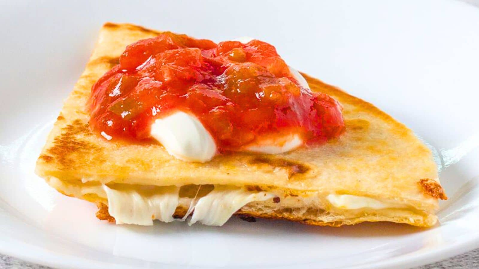 Cheese quesadilla quarter topped with sour cream and salsa