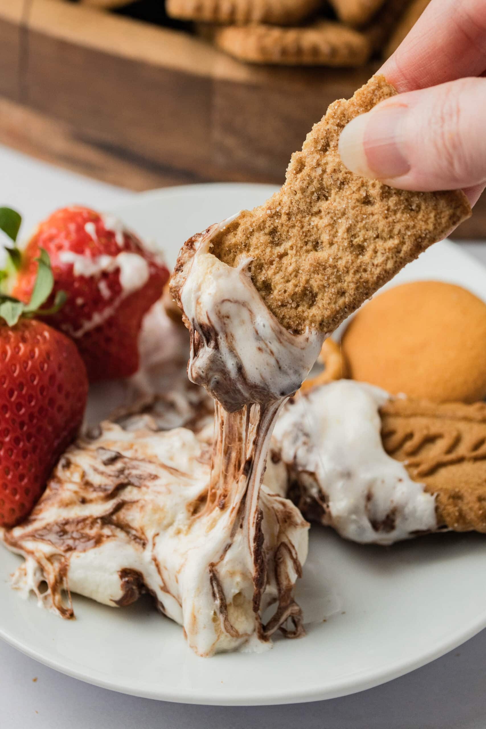 Hand holding graham cracker with melted chocolate and marshmallow on it