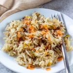 Dirty rice topped with hot sauce on a plate with a fork