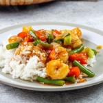 Hunan shrimp with green beans and red peppers over rice on a plate