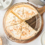Overhead view of a coconut meringue pie in glass dish on a wooden board
